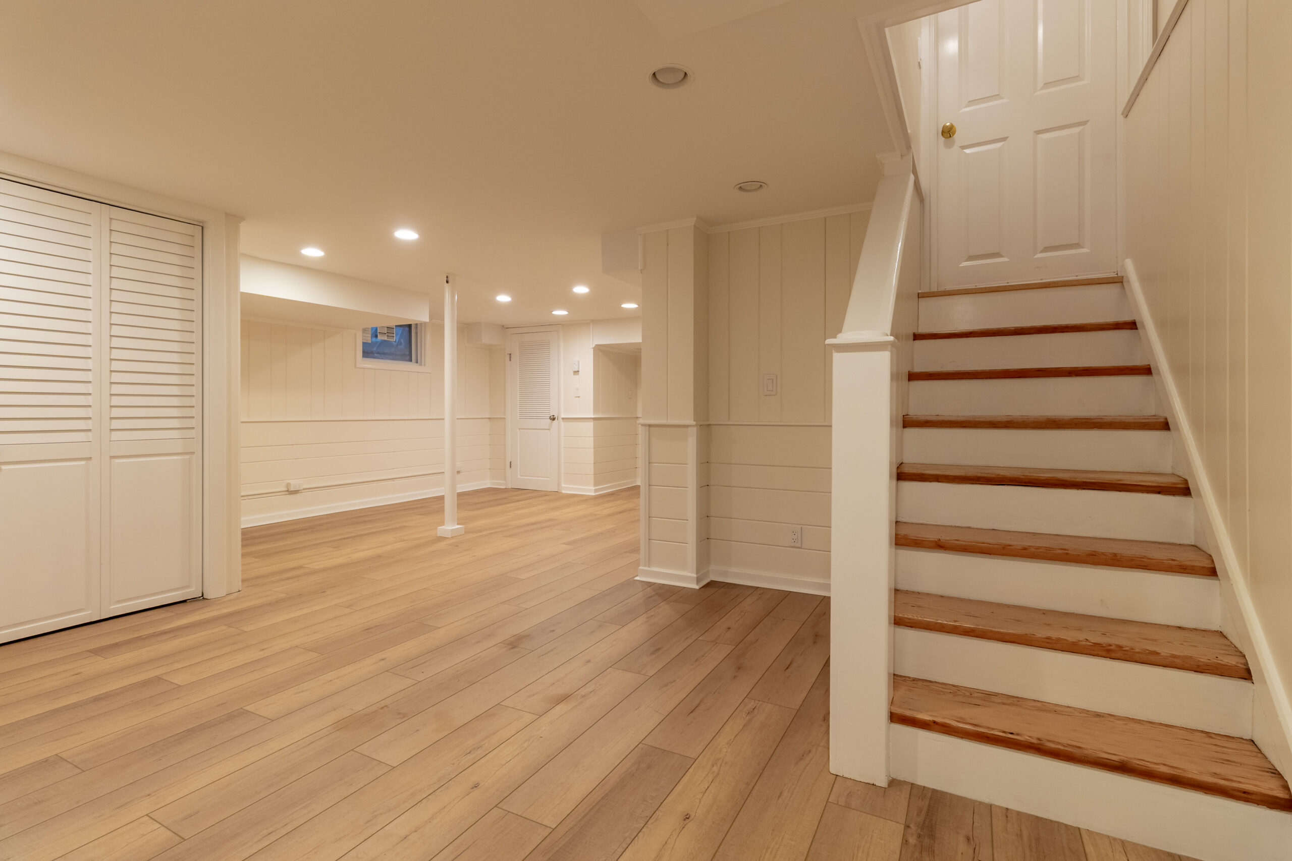 Finished basement renovation with wood flooring, white walls and staircase