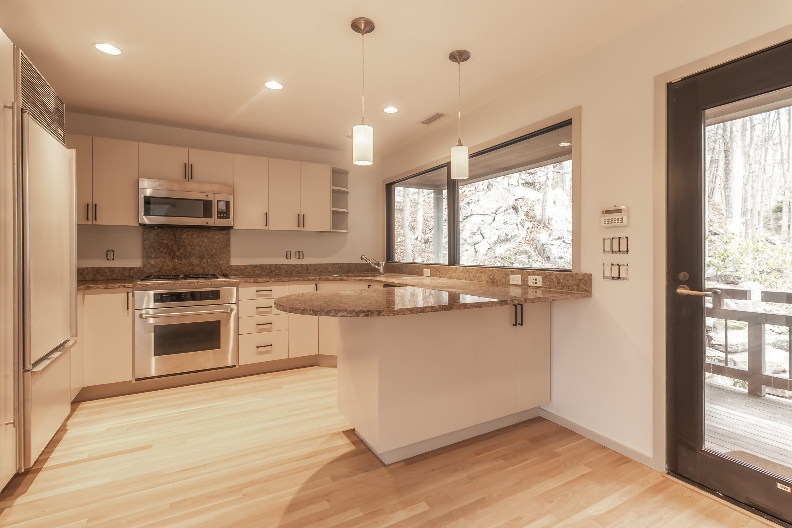 Renovated kitchen with light-colored cabinets, stone countertops and pendant lighting