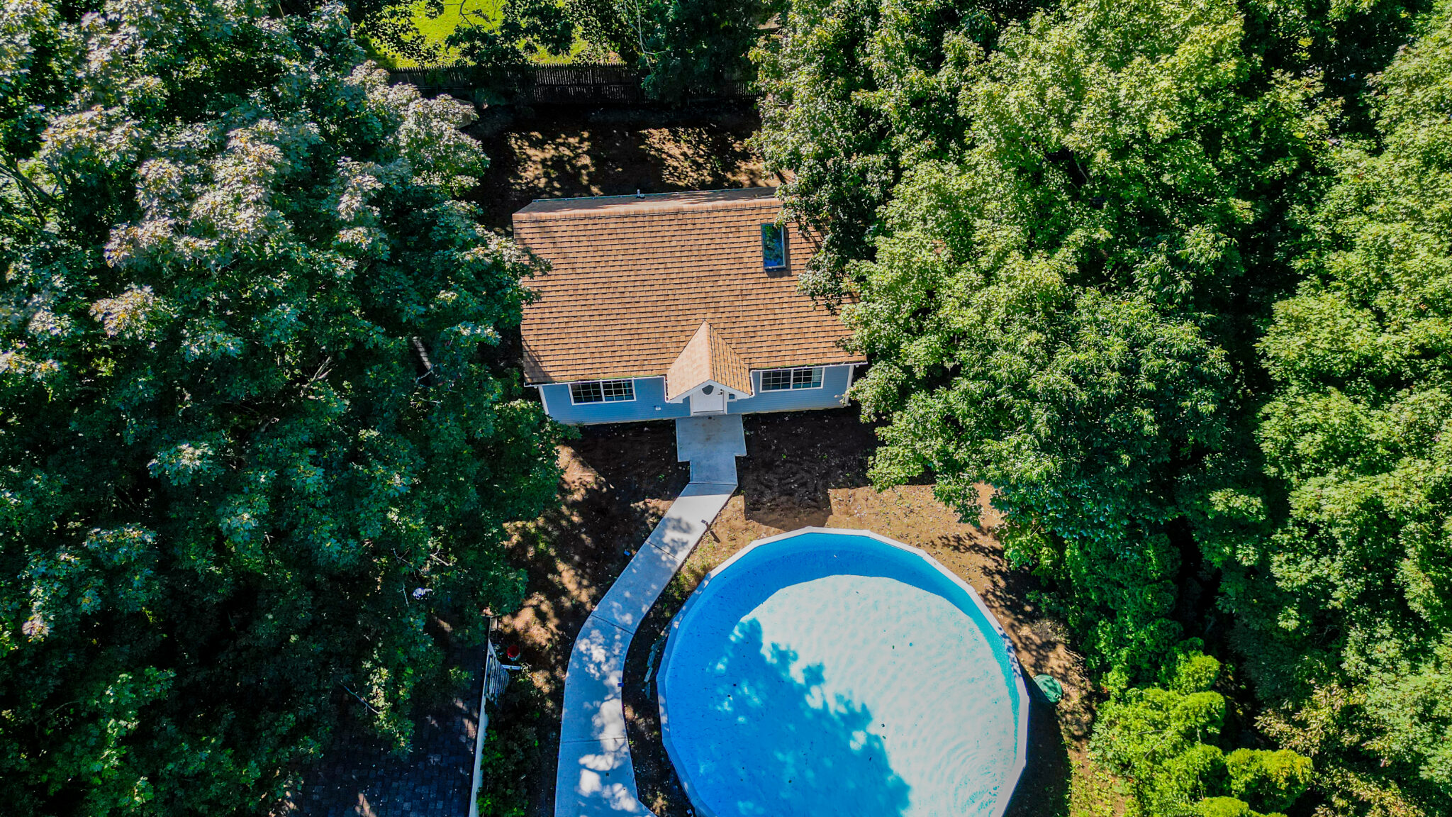 Overhead drone photograph of residential property with swimming pool, roof and surrounding trees in Groton, CT