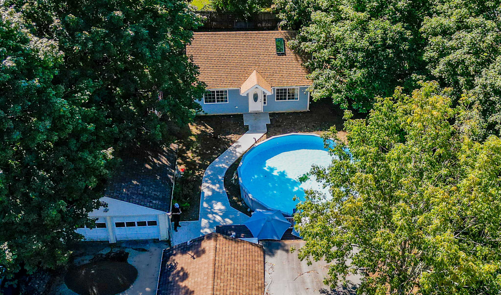 Aerial drone view of blue house, curved swimming pool, patio and surrounding trees in Groton, CT