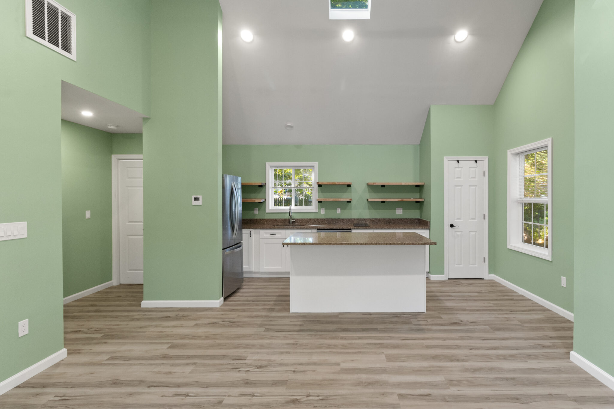 Finished open-plan kitchen and living area with green walls, white cabinets and wood-look flooring